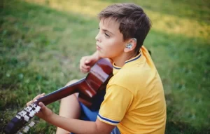 Child with a hearing aid playing the guitar
